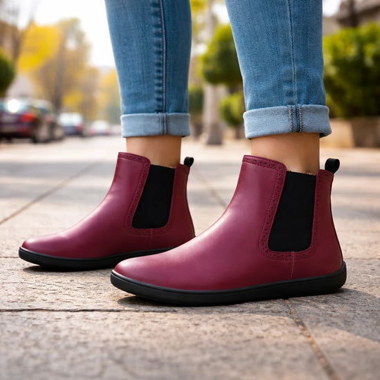 Mujer usando botas barefoot vinotinto en un entorno urbano, destacando la elegancia y confort.