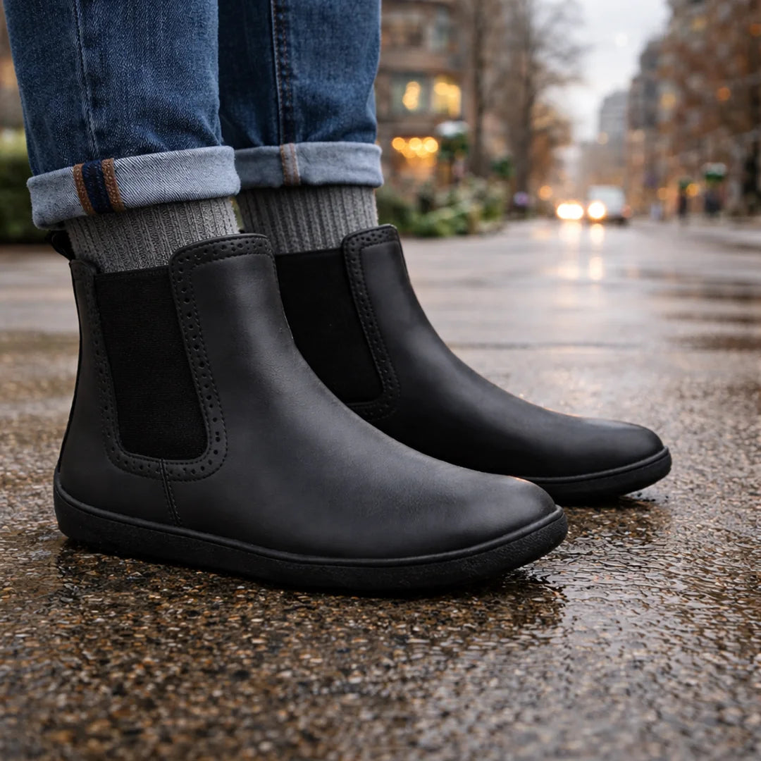 Botines minimalistas hombre casual negro Saguaro Urban I, calzado respetuoso urbano caminando sobre pavimento húmedo en Santiago.